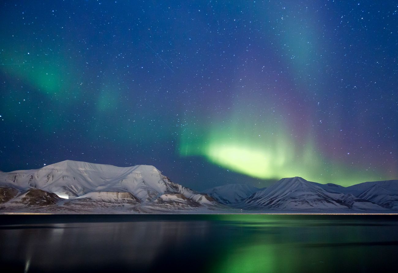 Green and purple Northern lights over the sea and mountains